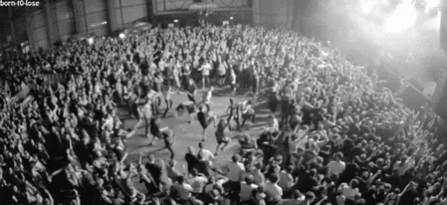 A Black And White Photo Of A Crowd Of People Dancing At A Concert GIF