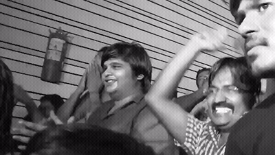 A Black And White Photo Of A Crowd With A Fire Extinguisher On The Wall Behind Them GIF
