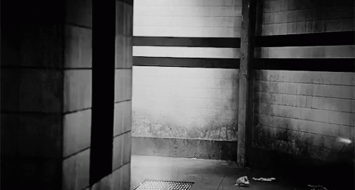 A Black And White Photo Of A Dark Room With A Brick Wall And A Drain . GIF