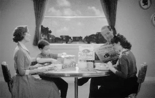 A Black And White Photo Of A Family Sitting At A Table Eating Food . GIF