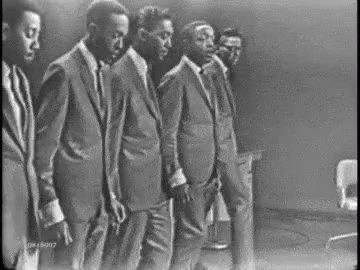 A Black And White Photo Of A Group Of Men In Suits And Ties Dancing . GIF