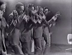 A Black And White Photo Of A Group Of Men Standing Next To Each Other In A Room . GIF
