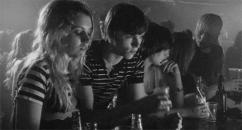 A Black And White Photo Of A Group Of People Sitting At A Table Drinking Beer GIF