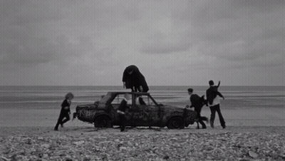 A Black And White Photo Of A Group Of People Standing Around A Car GIF