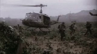A Black And White Photo Of A Helicopter Flying Over A Field Of Soldiers GIF