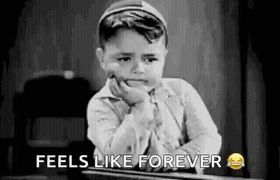 A Black And White Photo Of A Little Boy Sitting At A Desk With His Hand On His Face . GIF