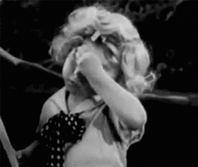A Black And White Photo Of A Little Girl Covering Her Face With Her Hands . GIF