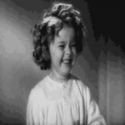 A Black And White Photo Of A Little Girl Smiling In A Room . GIF