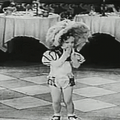 A Black And White Photo Of A Little Girl Standing On A Tiled Floor In Front Of A Table . GIF
