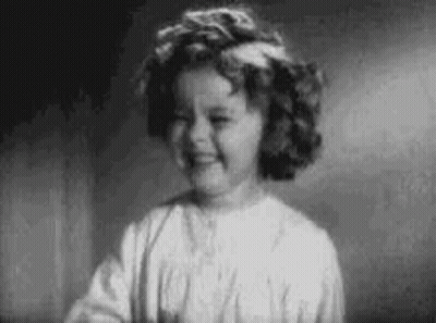A Black And White Photo Of A Little Girl With Curly Hair Smiling . GIF