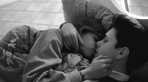 A Black And White Photo Of A Man And A Woman Kissing While Laying On A Bed . GIF
