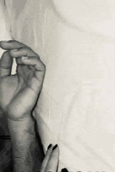 A Black And White Photo Of A Man And A Woman 'S Hands On A Bed . GIF
