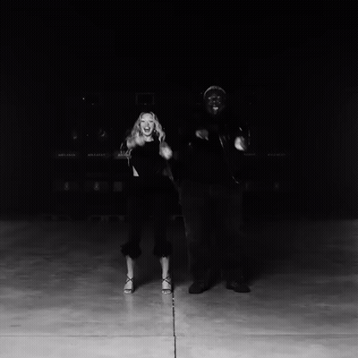 A Black And White Photo Of A Man And Woman Dancing In Front Of A Row Of Bellway Trucks GIF