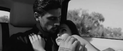 A Black And White Photo Of A Man And Woman Holding Hands In A Car . GIF