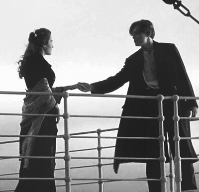 A Black And White Photo Of A Man And Woman Holding Hands On A Railing GIF