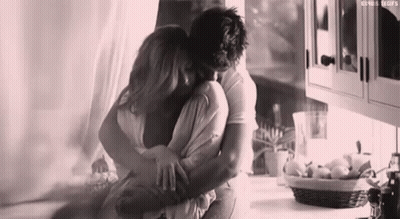 A Black And White Photo Of A Man And Woman Hugging In A Kitchen . GIF