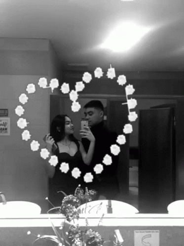 A Black And White Photo Of A Man And Woman Taking A Selfie In A Bathroom Mirror GIF
