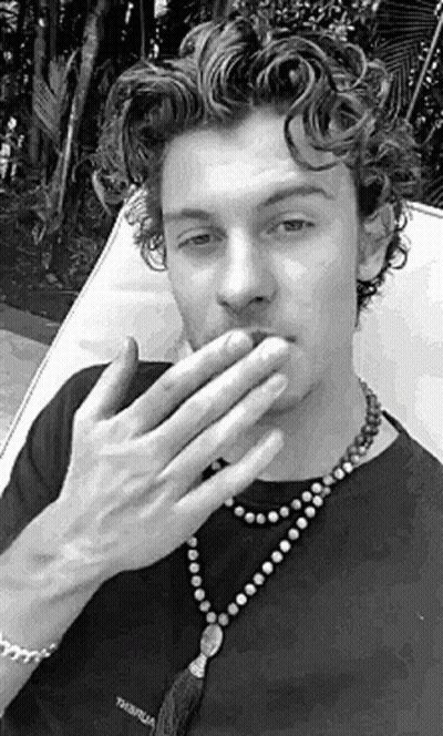 A Black And White Photo Of A Man Covering His Mouth With His Hands While Wearing A Necklace . GIF