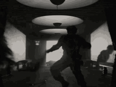 A Black And White Photo Of A Man Dancing In A Room With A Ceiling Light . GIF