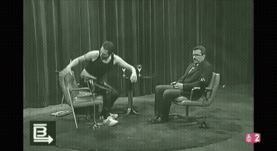 A Black And White Photo Of A Man Dancing In Front Of A Man Sitting In A Chair With The Number 2 On The Bottom GIF