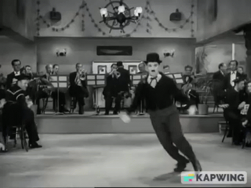 A Black And White Photo Of A Man Dancing In Front Of An Orchestra With Kapwing In The Corner GIF