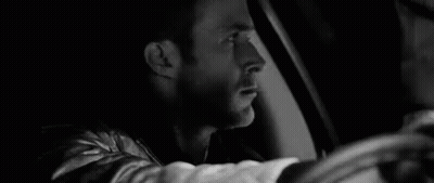 A Black And White Photo Of A Man Driving A Car At Night . GIF