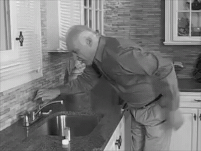 A Black And White Photo Of A Man Fixing A Sink Faucet In A Kitchen . GIF