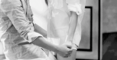 A Black And White Photo Of A Man Helping A Woman Tie Her Shirt . GIF