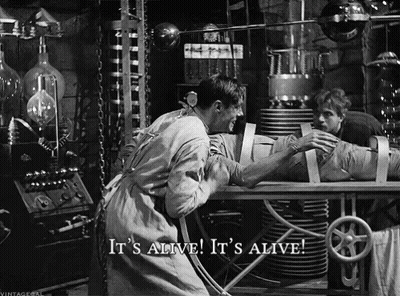 A Black And White Photo Of A Man Holding A Mummy With The Caption It 'S Alive It 'S Alive GIF