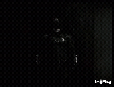 A Black And White Photo Of A Man In A Batman Costume Standing In The Dark . GIF