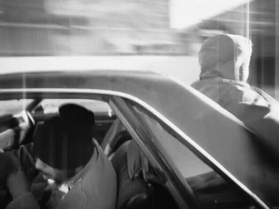 A Black And White Photo Of A Man In A Hoodie Driving A Car GIF