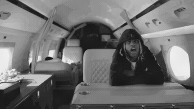 A Black And White Photo Of A Man In A Hoodie Sitting On A Plane . GIF