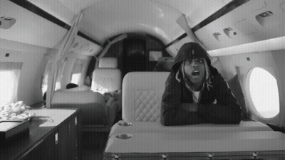A Black And White Photo Of A Man In A Hoodie Sitting On A Plane GIF