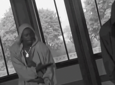 A Black And White Photo Of A Man In A Hoodie Standing In Front Of A Window GIF