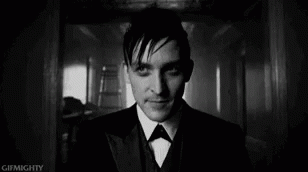 A Black And White Photo Of A Man In A Suit And Bow Tie Looking At The Camera . GIF