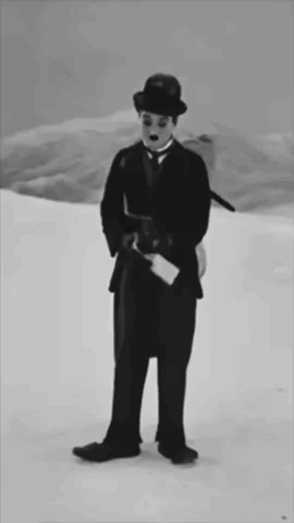 A Black And White Photo Of A Man In A Suit And Hat Standing In The Snow GIF
