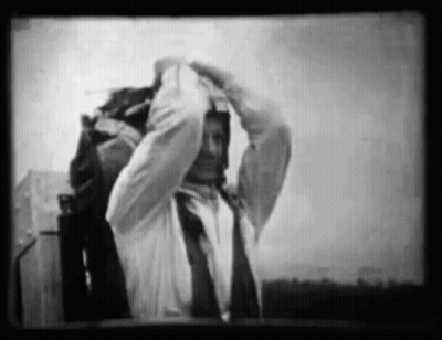 A Black And White Photo Of A Man In A Suit And Tie Adjusting His Tie . GIF