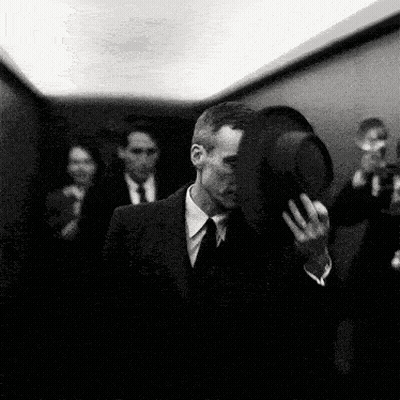 A Black And White Photo Of A Man In A Suit And Tie Holding A Hat GIF
