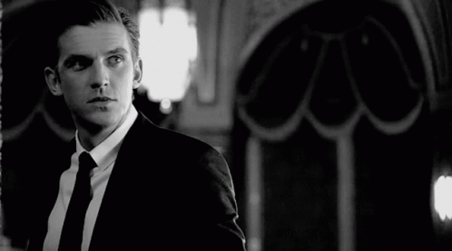 A Black And White Photo Of A Man In A Suit And Tie Looking At Himself In A Mirror . GIF