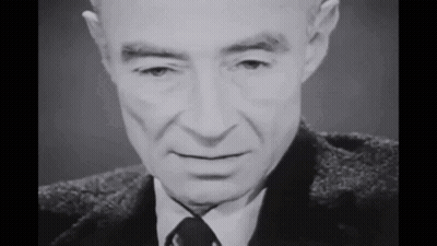 A Black And White Photo Of A Man In A Suit And Tie Looking At The Camera . GIF