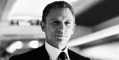 A Black And White Photo Of A Man In A Suit And Tie Looking At The Camera . GIF