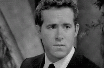 A Black And White Photo Of A Man In A Suit And Tie Making A Face . GIF