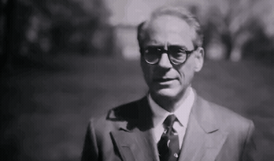 A Black And White Photo Of A Man In A Suit And Tie Standing In A Park . GIF