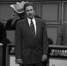 A Black And White Photo Of A Man In A Suit And Tie Standing In Front Of A Sign That Says Jeopardy . GIF