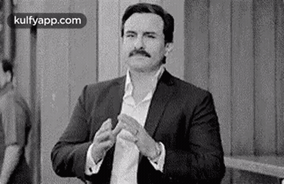 A Black And White Photo Of A Man In A Suit Clapping His Hands . GIF