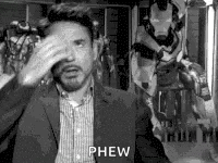 A Black And White Photo Of A Man In A Suit Covering His Face With His Hands . GIF