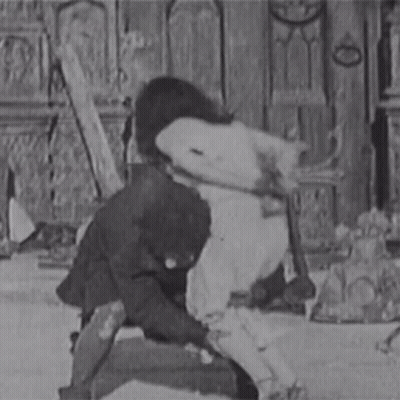 A Black And White Photo Of A Man In A Suit Holding A Woman 'S Leg . GIF