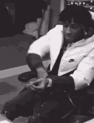 A Black And White Photo Of A Man In A Suit Sitting In A Chair . GIF