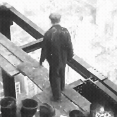 A Black And White Photo Of A Man In A Suit Standing On A Bridge . GIF