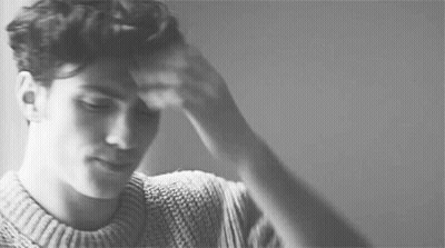 A Black And White Photo Of A Man In A Sweater Holding His Head . GIF